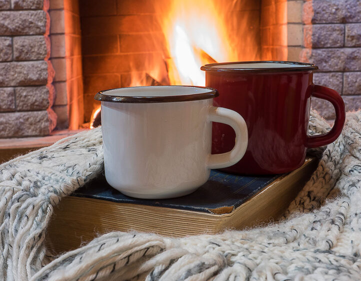 Cozy scene before fireplace with two enameled mugs of tea, a boo