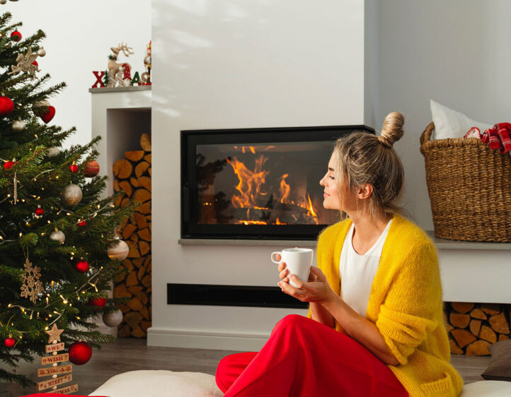 Happy woman sits beside a fireplace in a cozy living room, adorn